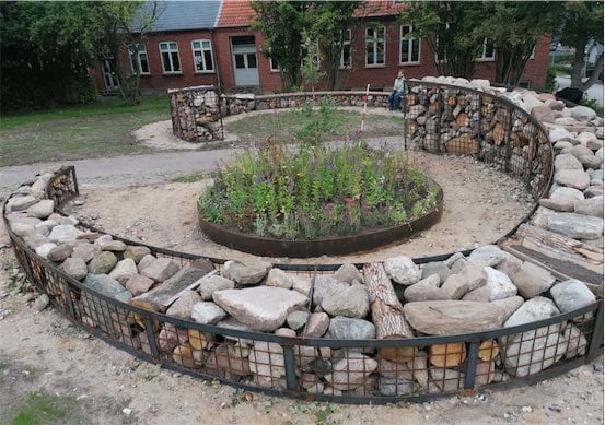 Rund stenhave foran murstensbygning med planter i midten