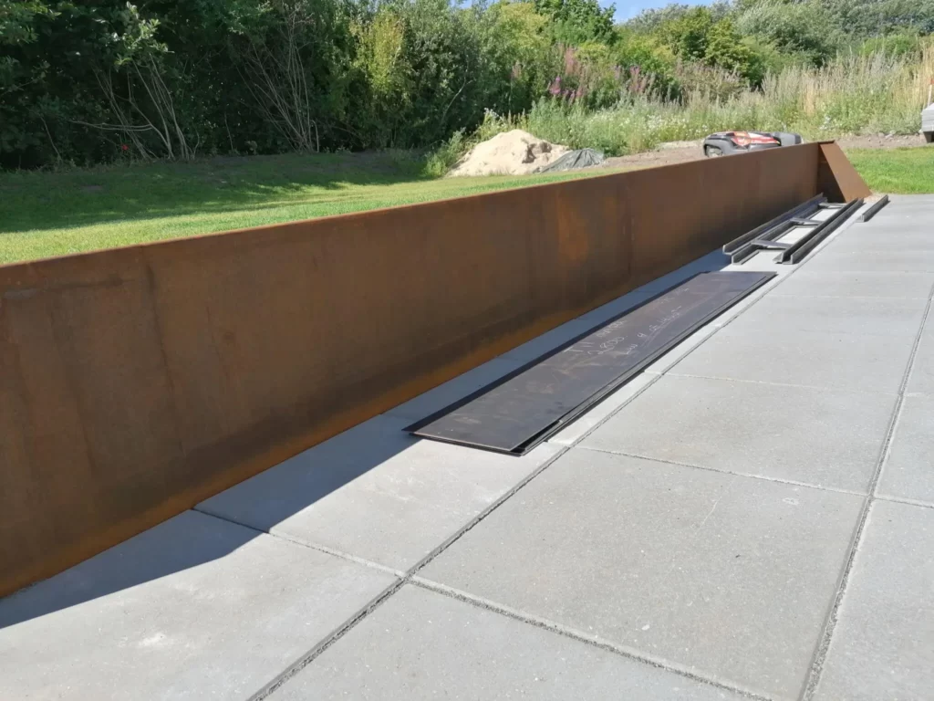 Rusten stålvæg langs flisebelagt terrasse