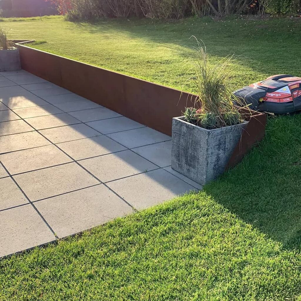 Flisebelagt terrasse med græsplæne og plantekasse