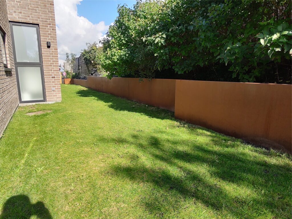 Grøn have ved murstenshus med sol og buske