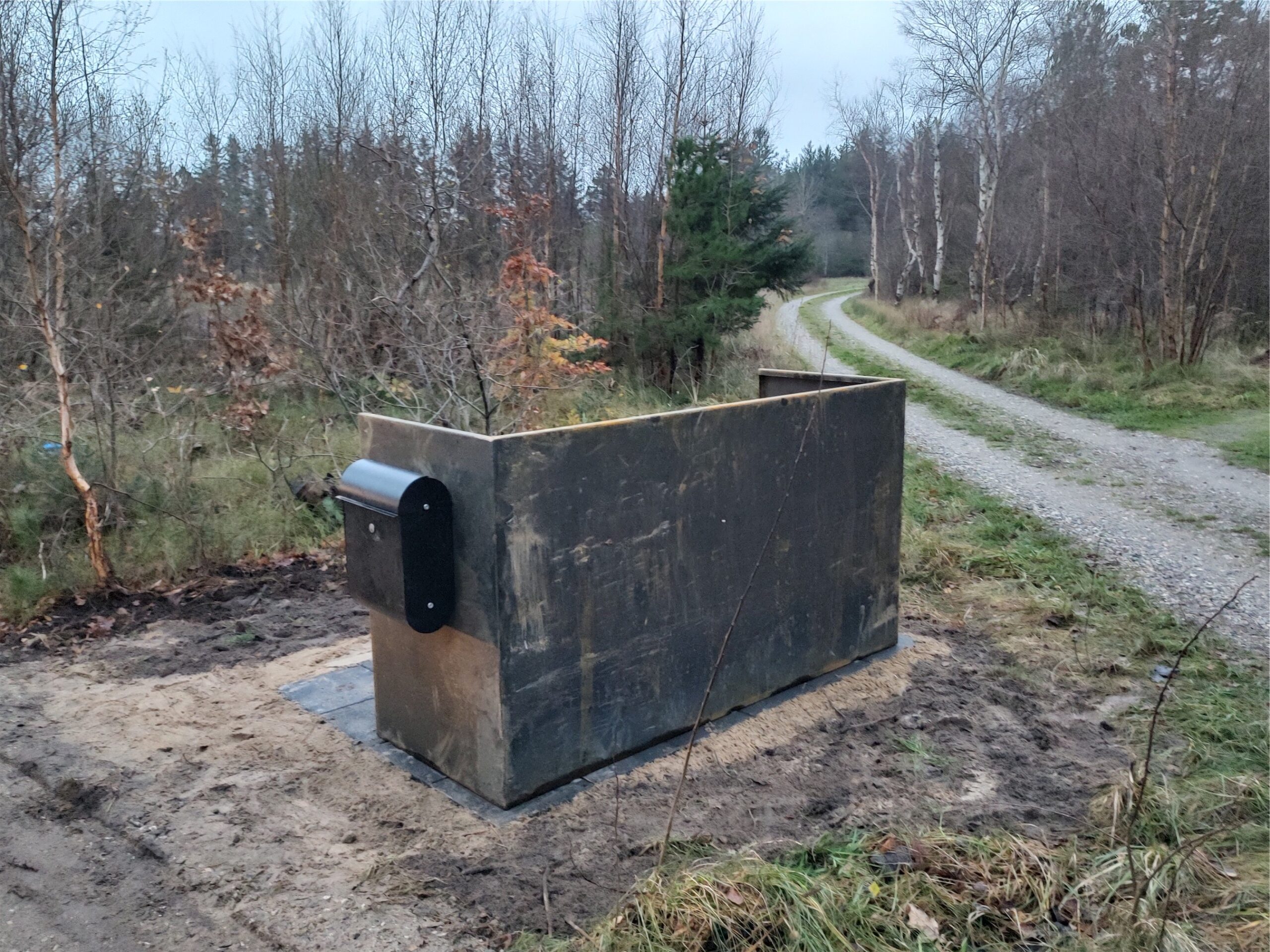 Affaldscontainer ved grusvej i skovområde