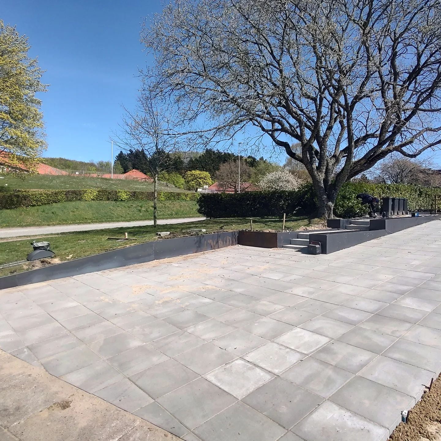 Nybygget terrasse med fliser og stort træ i haven