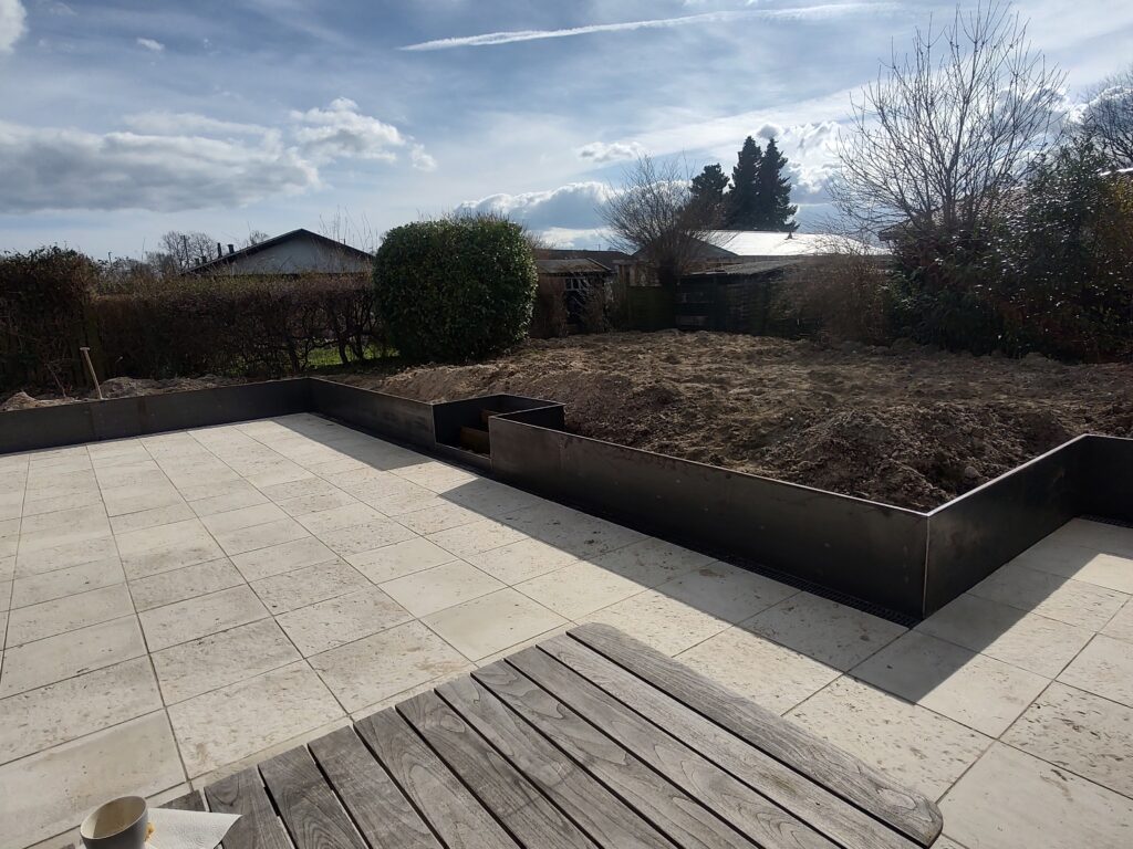 Ny flisebelagt terrasse med hævet bed i haven