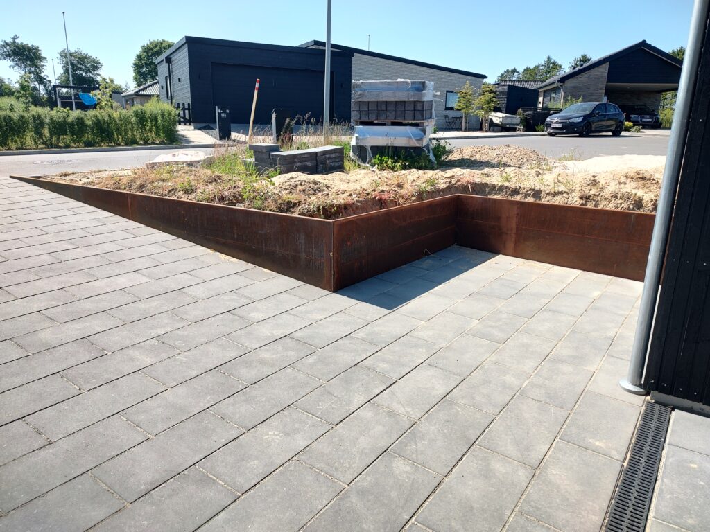 Hævet bed med cortenstål og flisebelægning foran hus
